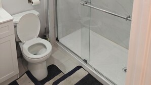 A bathroom with a glass-enclosed shower, a toilet, and a sink.