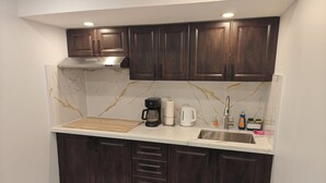 A compact kitchen with dark wood cabinets, a marble backsplash, and a stainless steel sink.