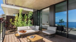 A modern outdoor living area with a sofa, armchair, and coffee table, overlooking a balcony with a view of the ocean. - Savoy Monumentalis VII – Comfort & Luxury (Funchal)