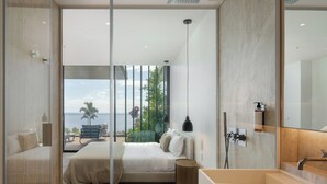 A modern bedroom with a large bed, a bedside table, a nightstand, a bathroom with a sink and mirror, and a view of the outdoors. - Savoy Monumentalis VII – Comfort & Luxury (Funchal)