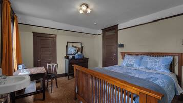 A bedroom with a wooden bed, a dresser, a mirror, a desk with a chair, and a bathroom with a sink and toilet.