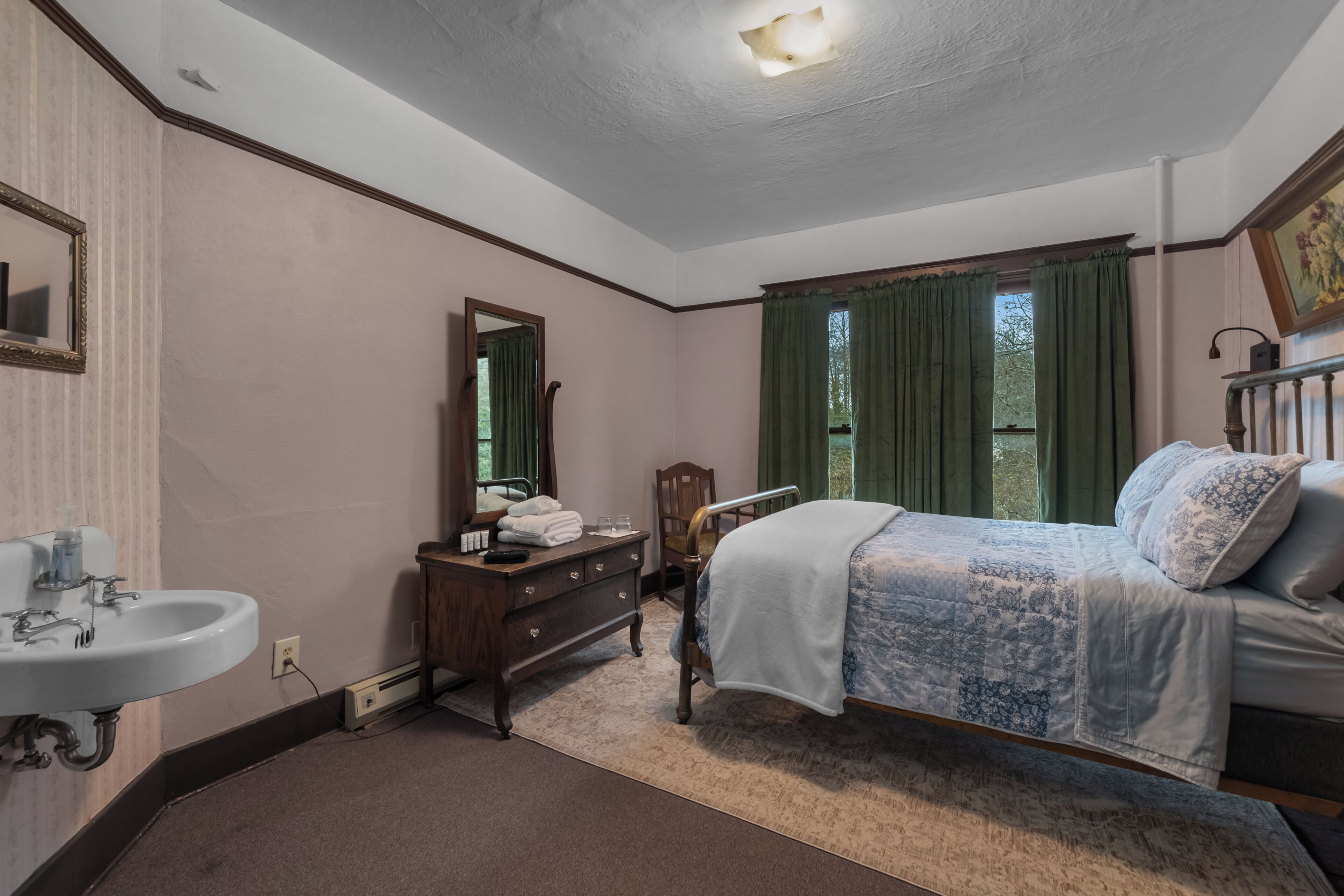 A bedroom with a bed, a dresser, a mirror, a sink, and a window with curtains.