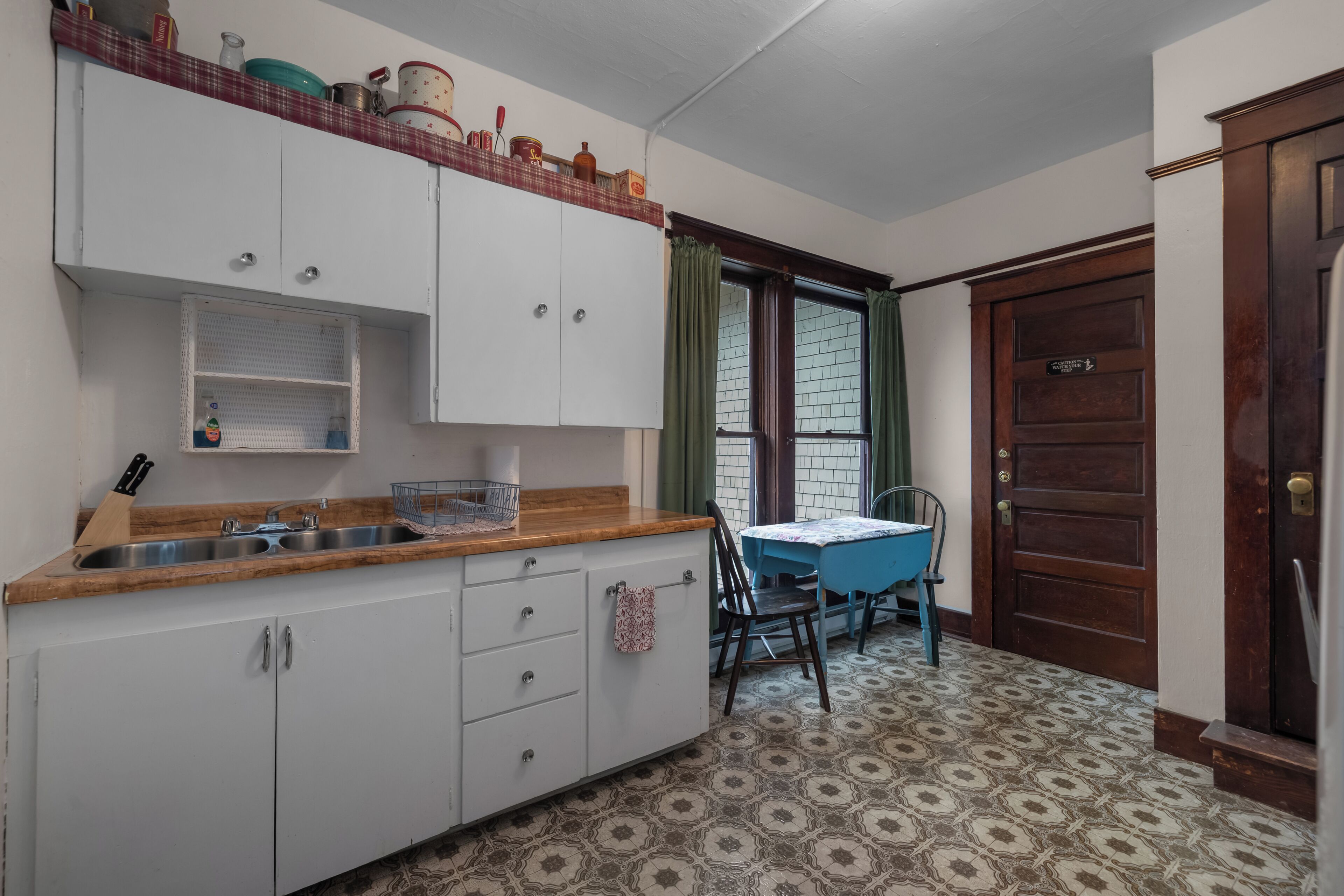 Une cuisine avec un plan de travail en bois, des placards blancs, un évier et une table à manger avec des chaises.