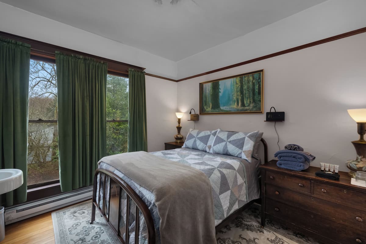 A bedroom with a bed, a dresser, a nightstand, a painting, and a window with curtains.