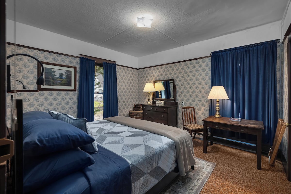 A bedroom with a bed, dresser, desk, chair, and a window with curtains.