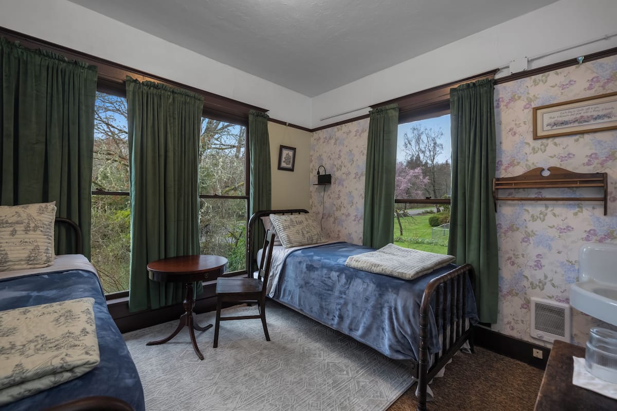 A room with two beds, a chair, a small table, and a window with curtains.