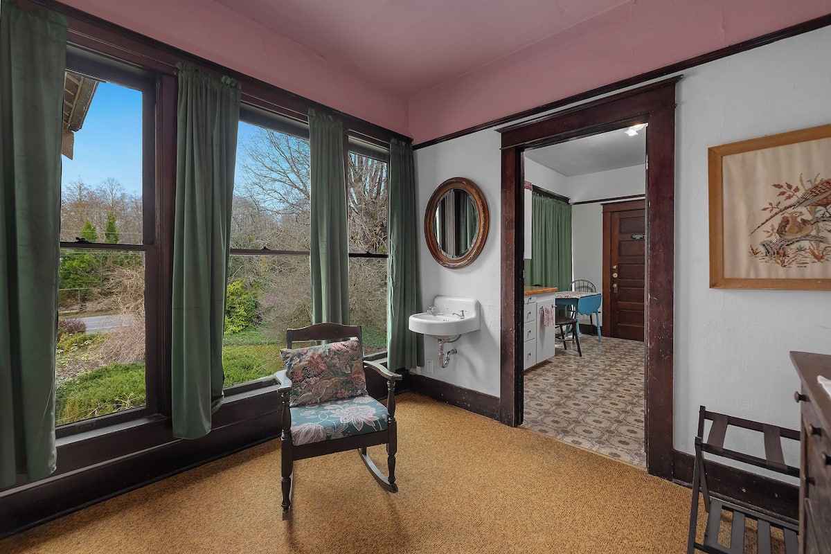 A room with a rocking chair, a sink, and a view through large windows.