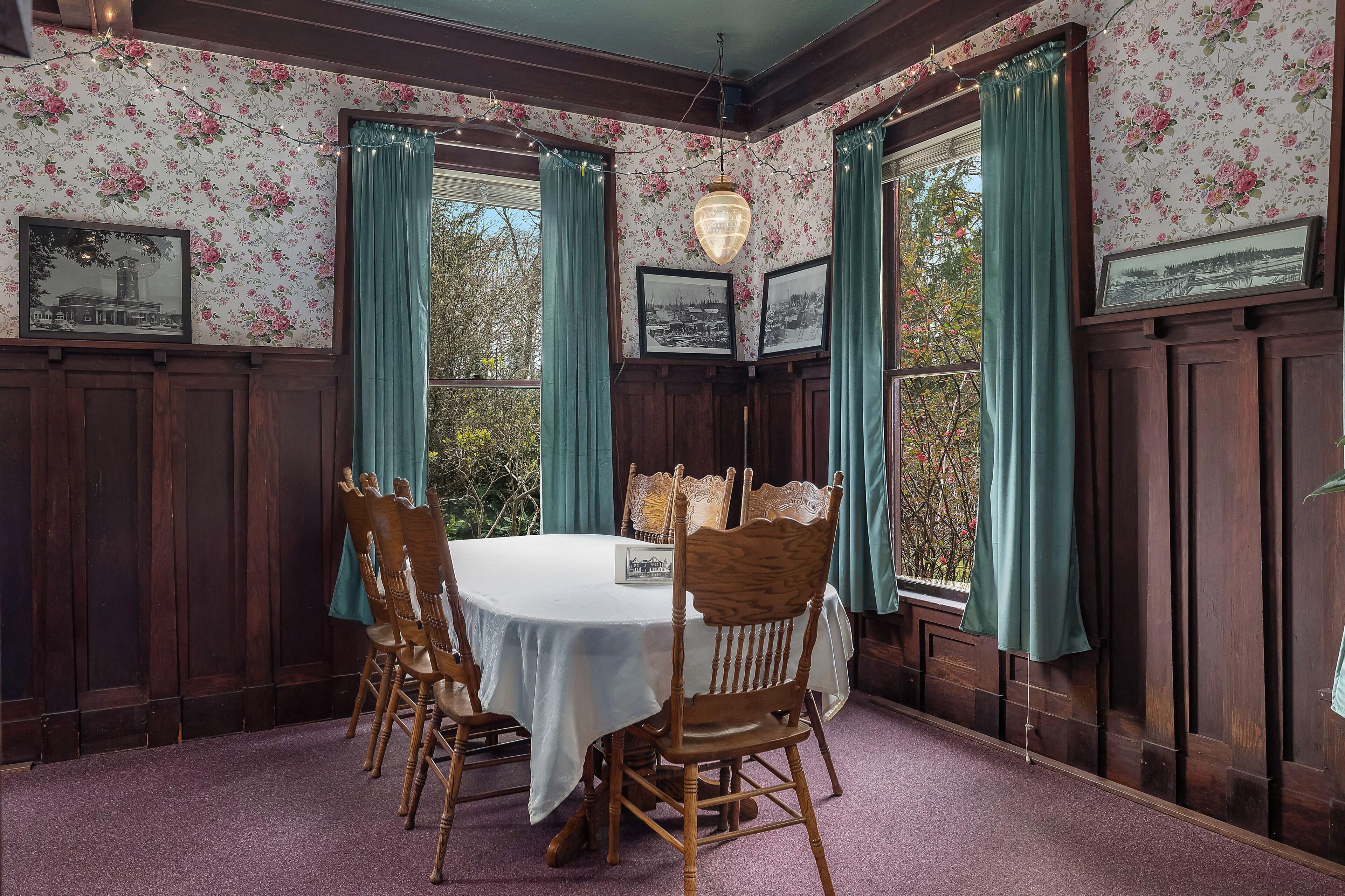 A dining area with a round table, wooden chairs, floral wallpaper, and framed pictures on the walls.