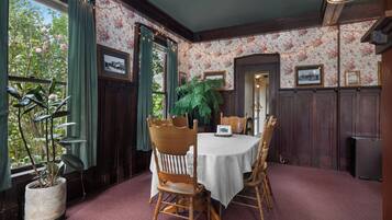 Comedor con una mesa redonda, sillas de madera, una planta en maceta y papel tapiz con motivos florales.