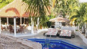Un área de piscina con sillones de descanso y una estructura de techo de paja.