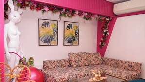 Ein Zimmer mit einer rosafarbenen Wand, einem sofa mit floralem Muster, einer weißen Statue und zwei gerahmten Gemälden.