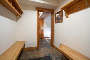 Un couloir avec des bancs en bois, une porte donnant sur une autre pièce et un tableau accroché au mur.