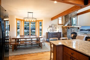 A kitchen with a stone fireplace, wooden beams, and a dining area with a large table and chairs.