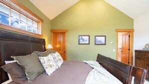 A bedroom with a large bed, wooden headboard, two framed pictures on the wall, and a wooden door. - Moonstone Lodge • Hot Tub • Spacious (Breckenridge)