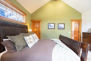 Une chambre à coucher avec un grand lit, une tête de lit en bois, deux tableaux encadrés accrochés au mur et une porte en bois.