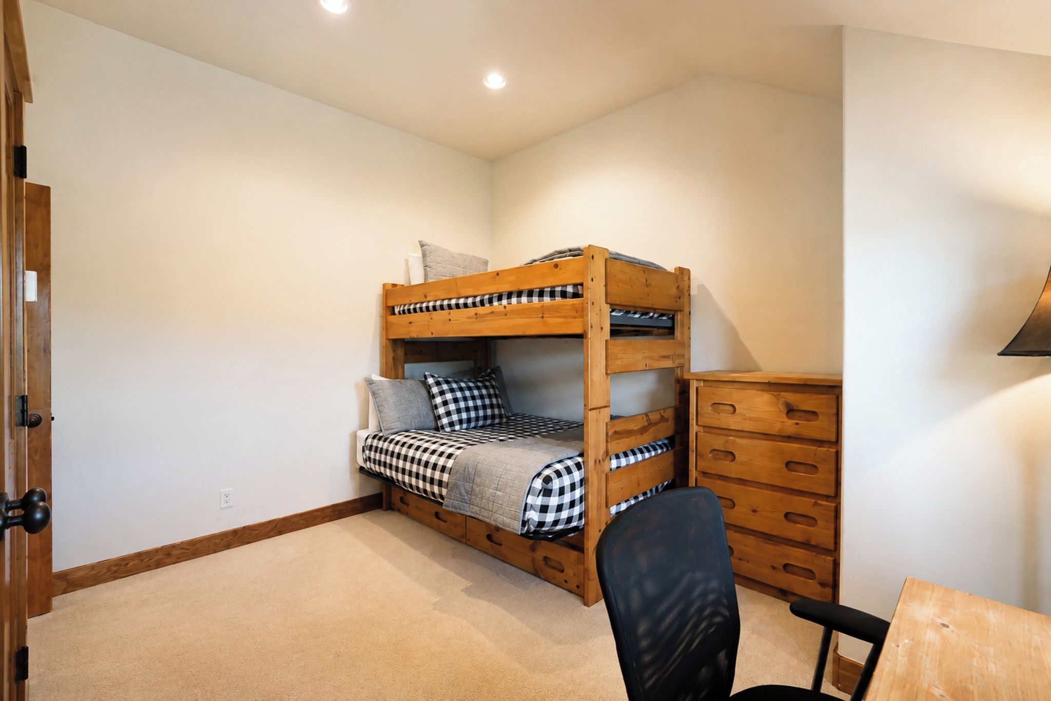 A bunk bed with a desk and chair, a dresser, and a door.