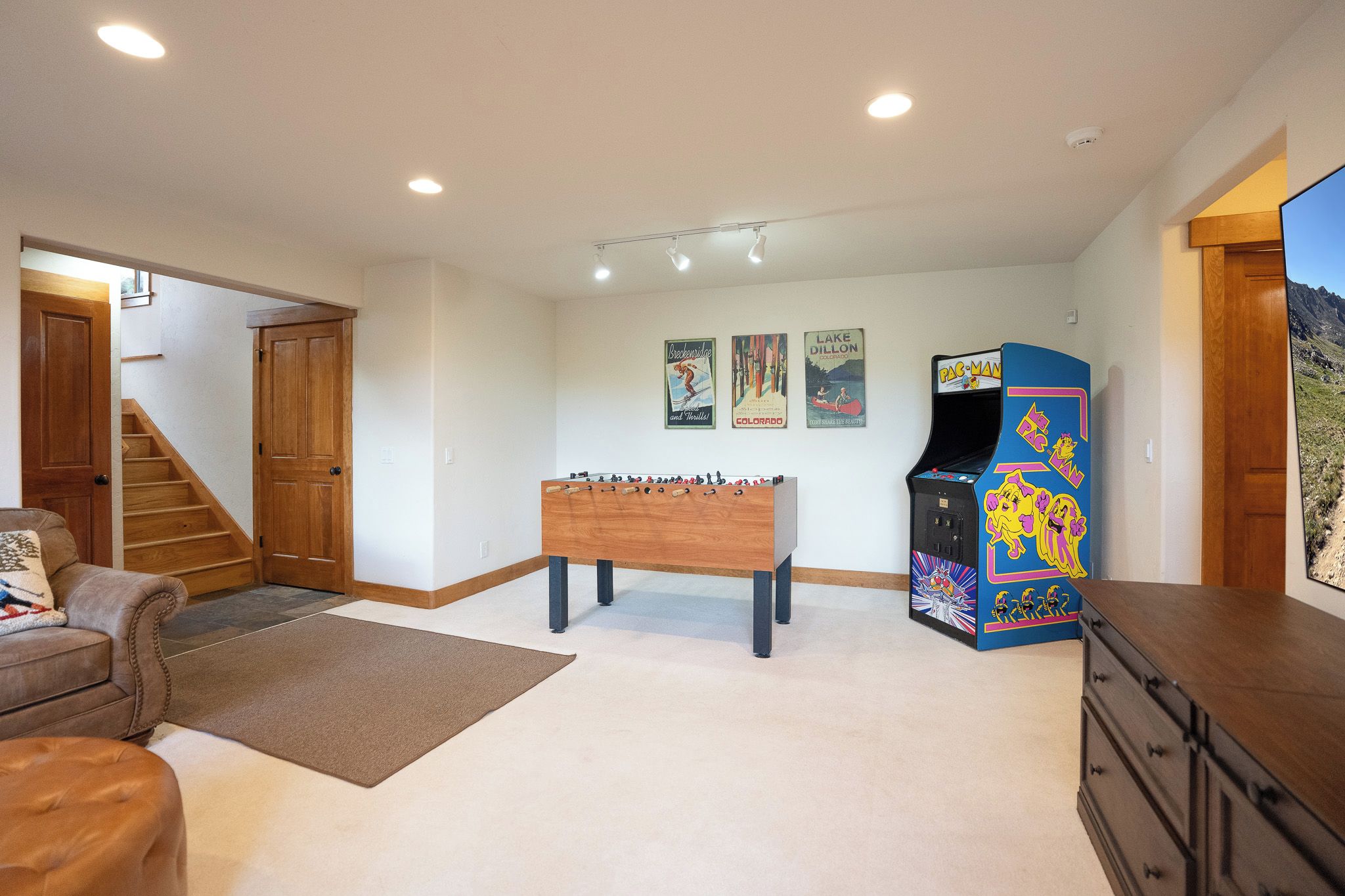A room with a foosball table, a pinball machine, a sofa, and a staircase.