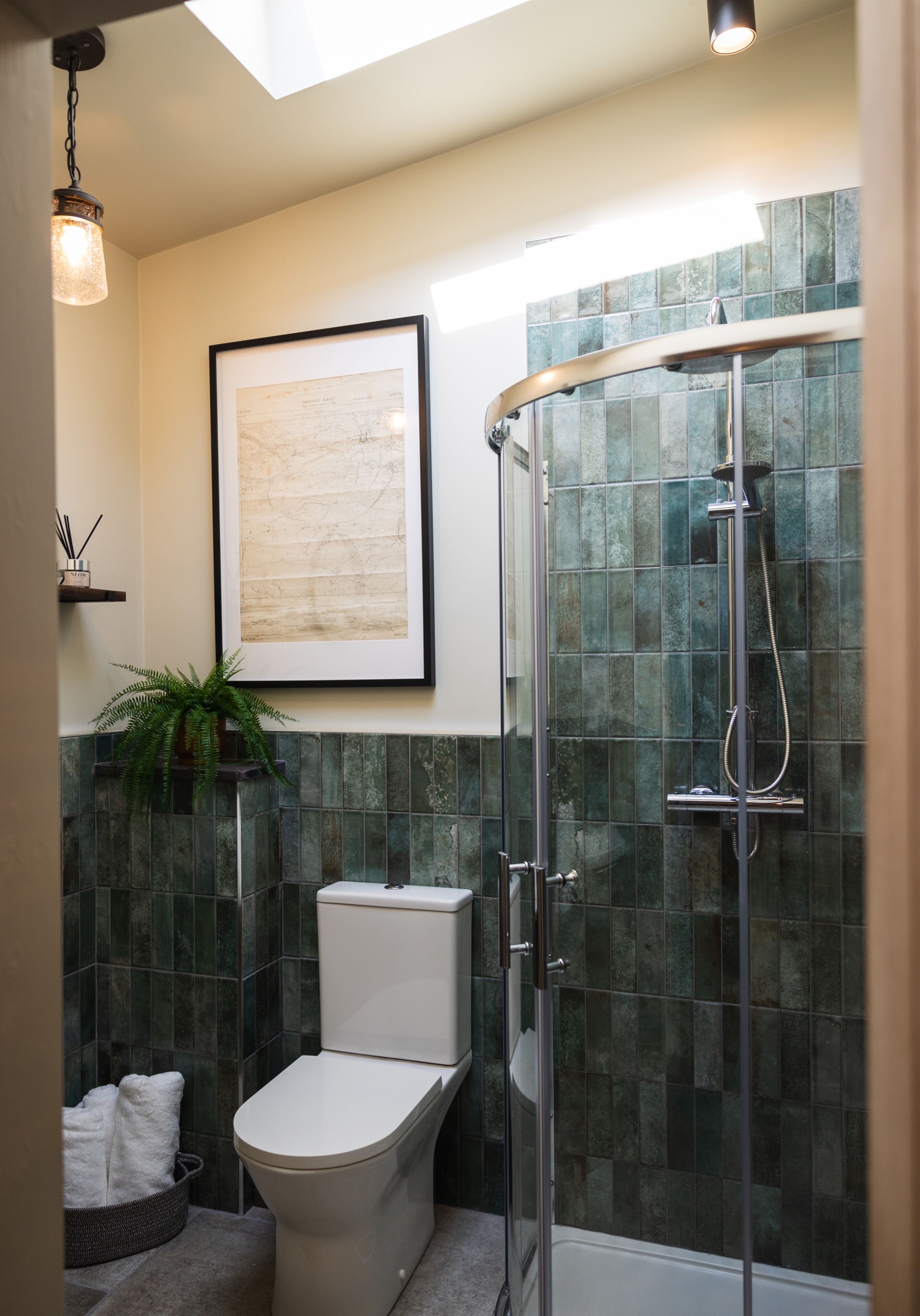 A modern bathroom with a glass-enclosed shower, a toilet, and a framed artwork on the wall.