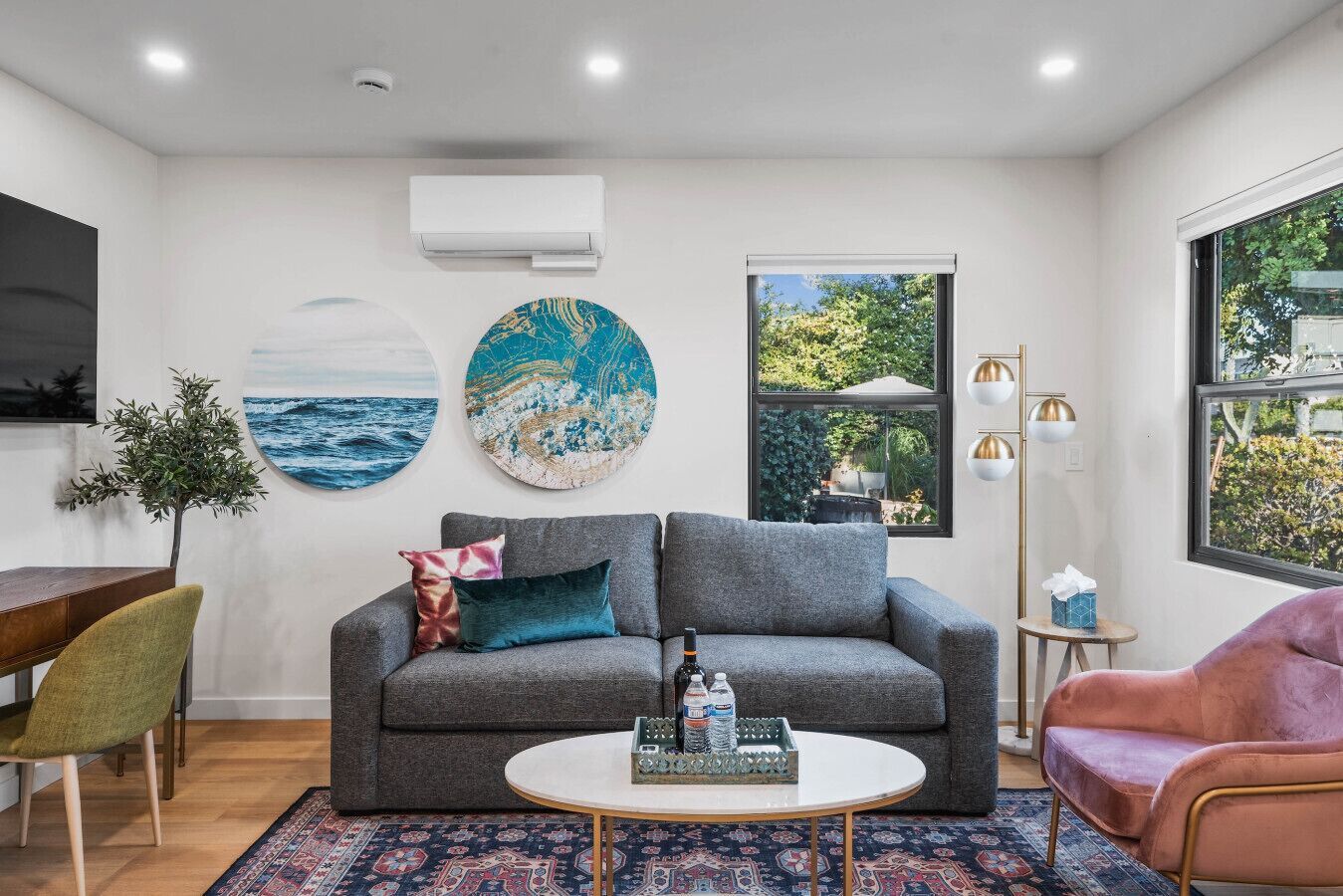 A modern living room with a grey sofa, a round coffee table, and a view of greenery outside.