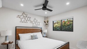 Camera da letto moderna con un letto in legno, una ventola a soffitto, una finestra con vista sul giardino e decorazioni murali.