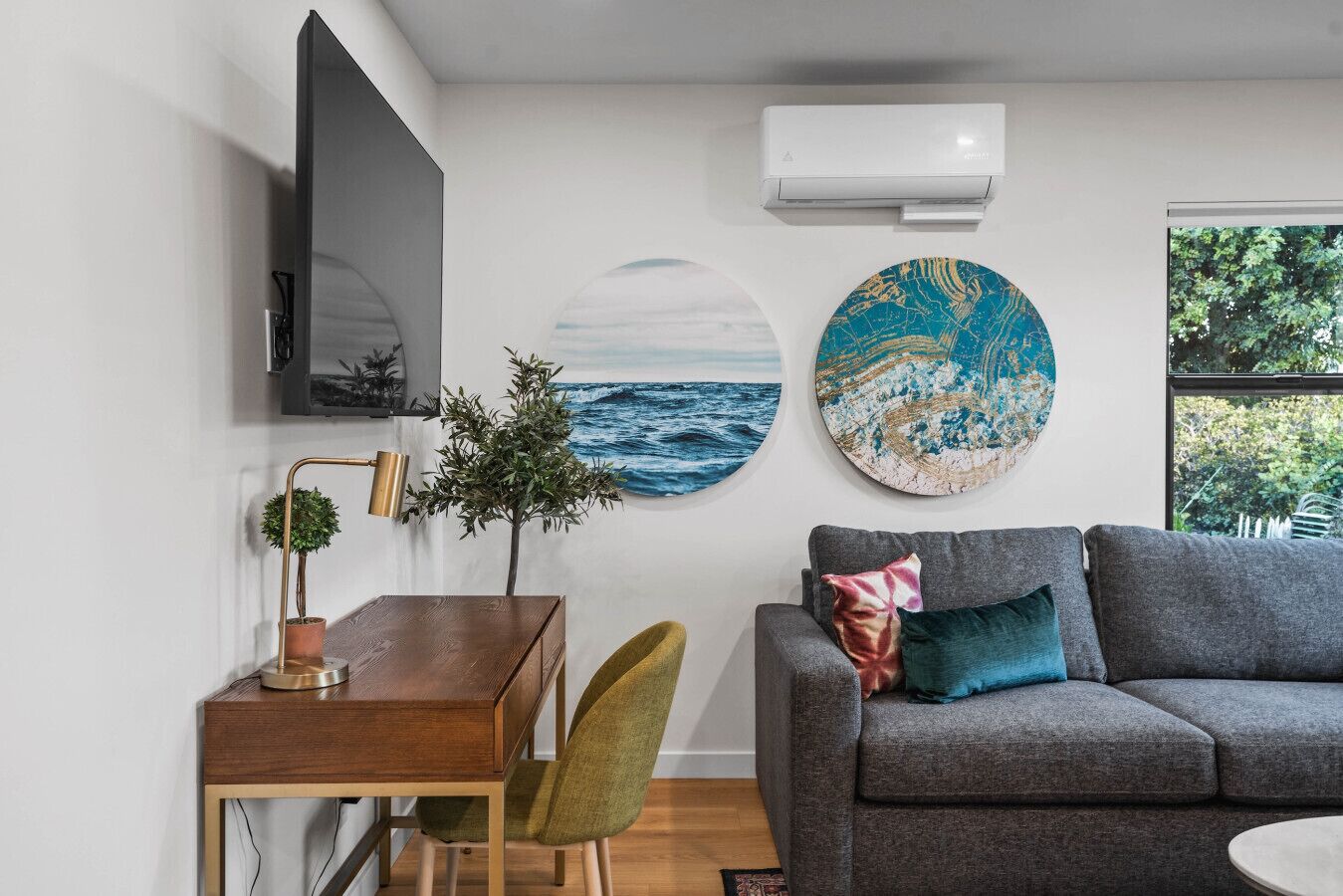 Ein modernes Wohnzimmer mit grauem Sofa, einem Holzesstisch, einem grünen Sessel, einem Fernseher und Kunstwerken an den Wänden.