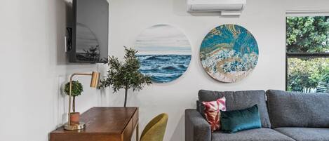 Ein modernes Wohnzimmer mit grauem Sofa, einem Holzesstisch, einem grünen Sessel, einem Fernseher und Kunstwerken an den Wänden.