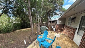 A wooden deck with blue chairs, a covered grill area, and a brick wall. - Charming SE ICT Home 3 Bedrooms/2 Baths/2 Queens/1 Twin/1 Queen Pullout (Wichita)