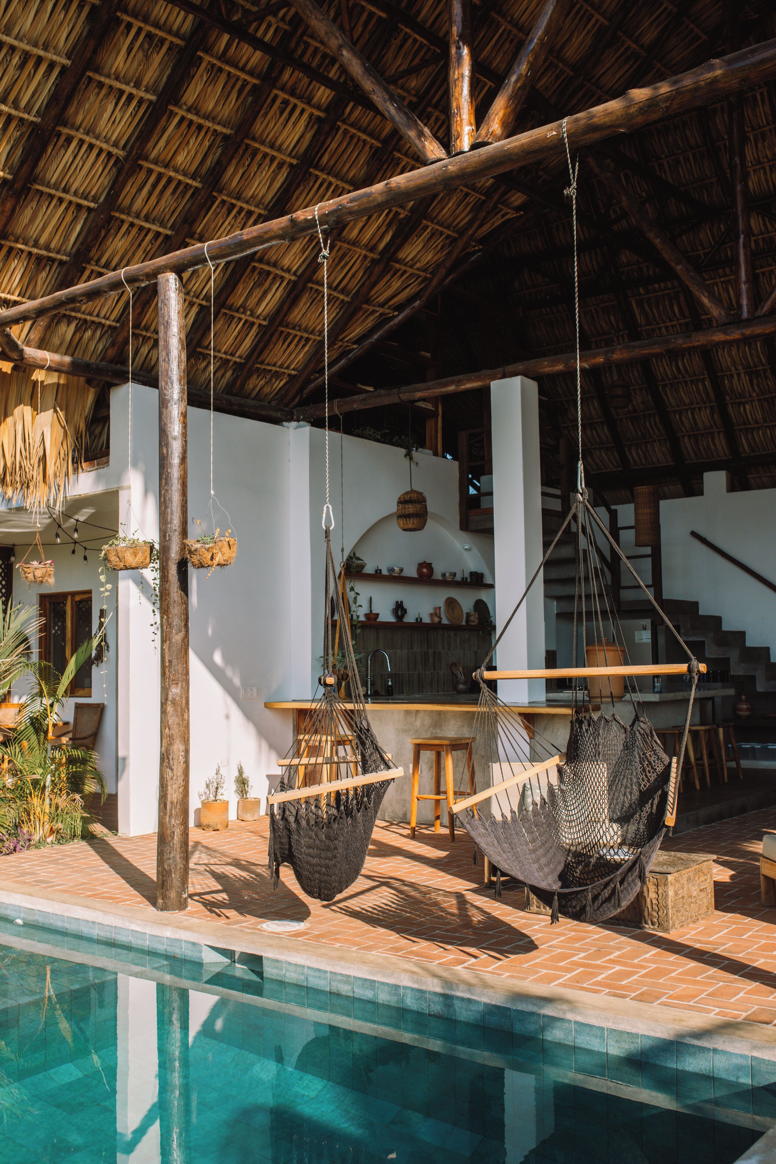 A pool area with hanging hammocks, a thatched roof, and a staircase leading to an upper level.