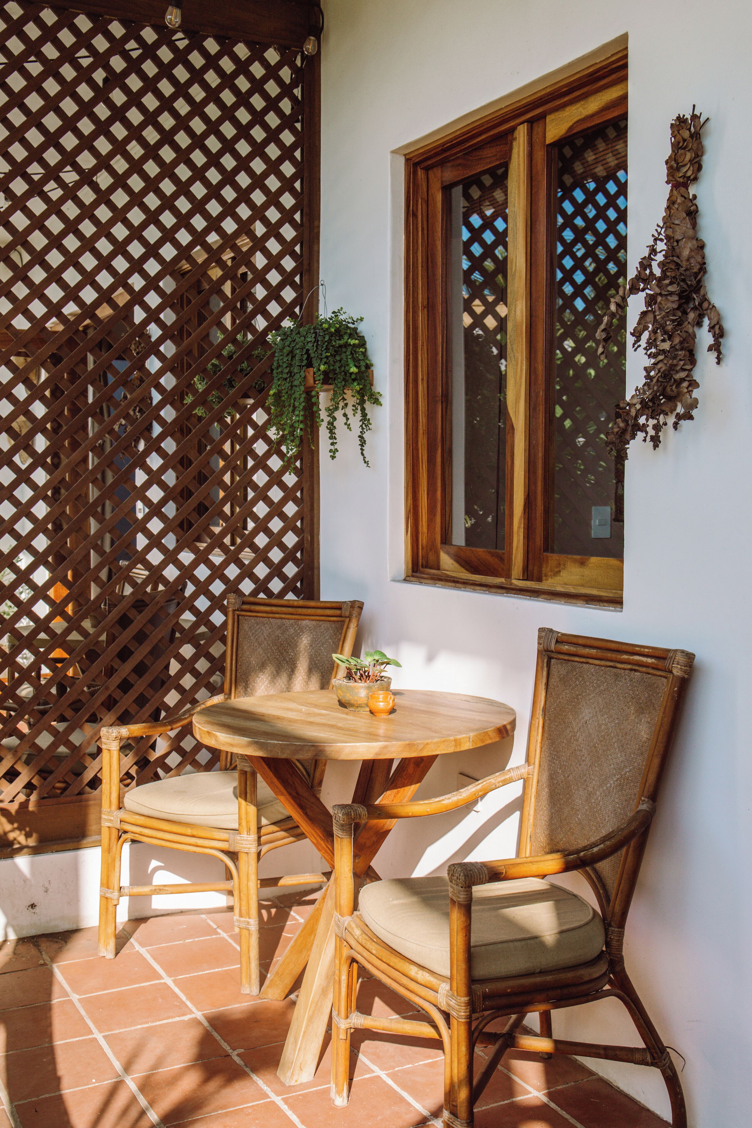 A wooden table and two chairs in a corner, with a lattice screen and a window with a wooden frame.