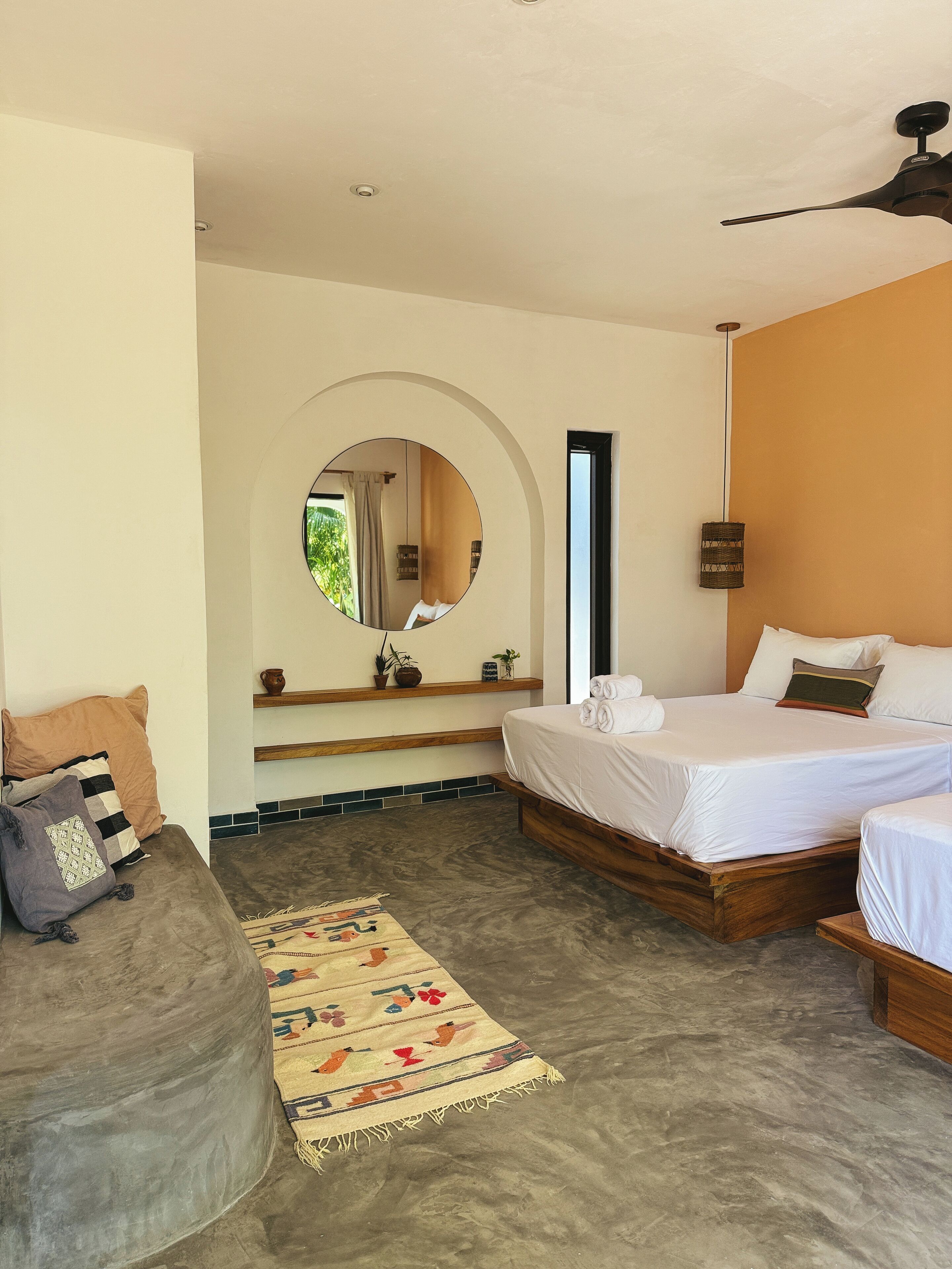 Un dormitorio con cama, sofá, espejo y ventilador de techo.