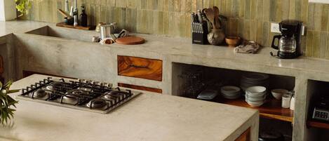A kitchen with a central island, wooden stools, and shelves with plants and kitchenware.
