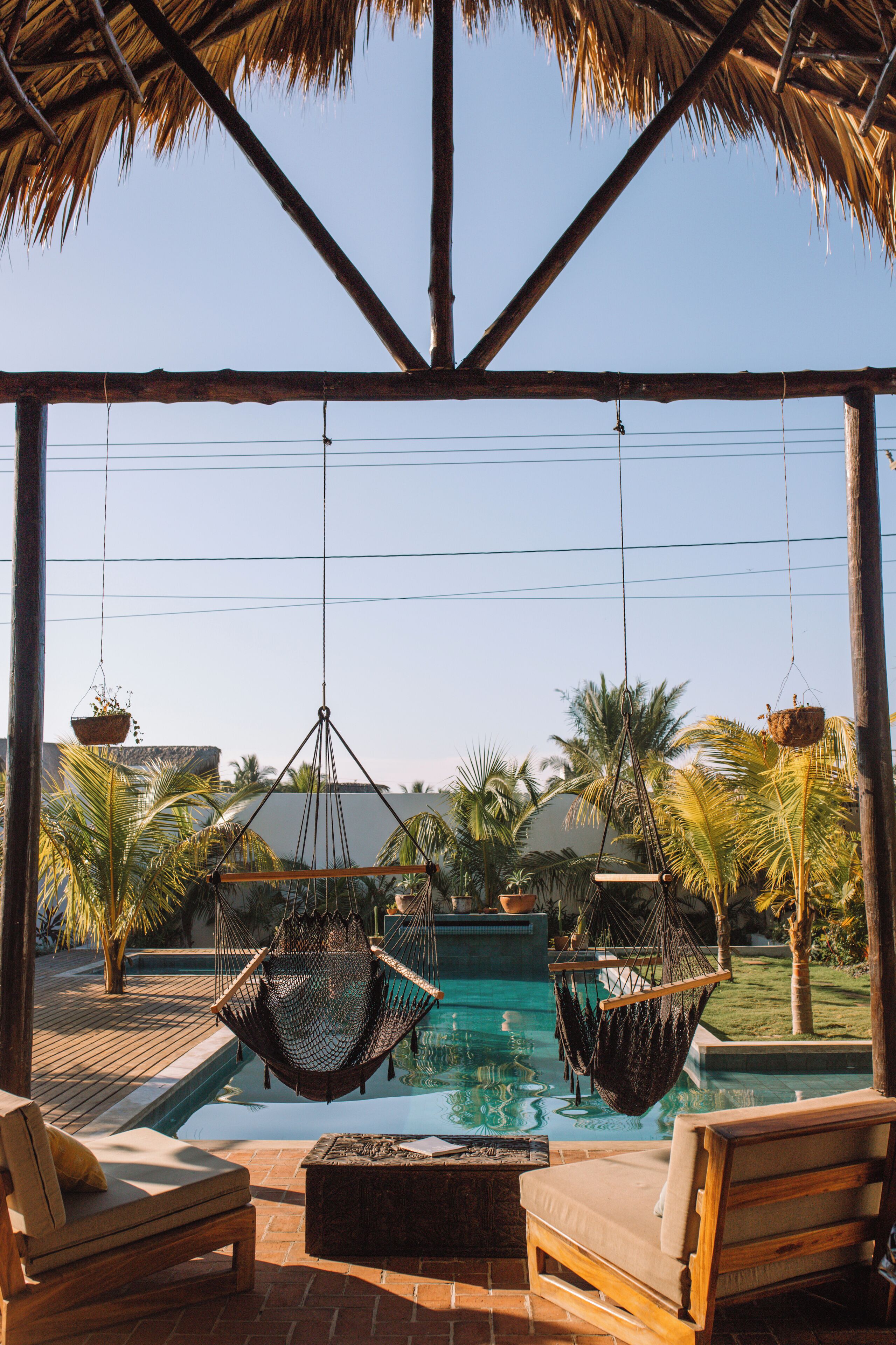Un área de piscina con dos sillones de madera, una hamaca y un macramé colgante.