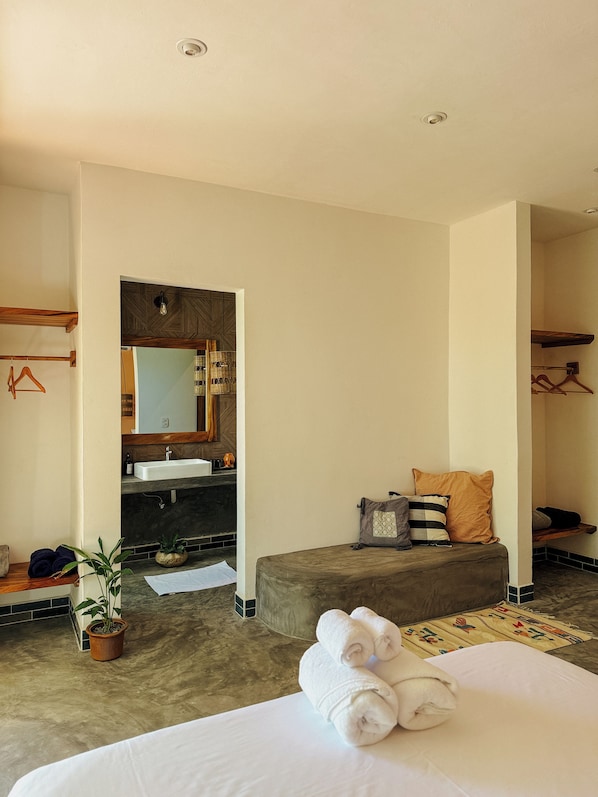 A hotel room with a bed, a bathroom with a sink and mirror, a small seating area, and a potted plant. - Casa Zala (Sipacate)