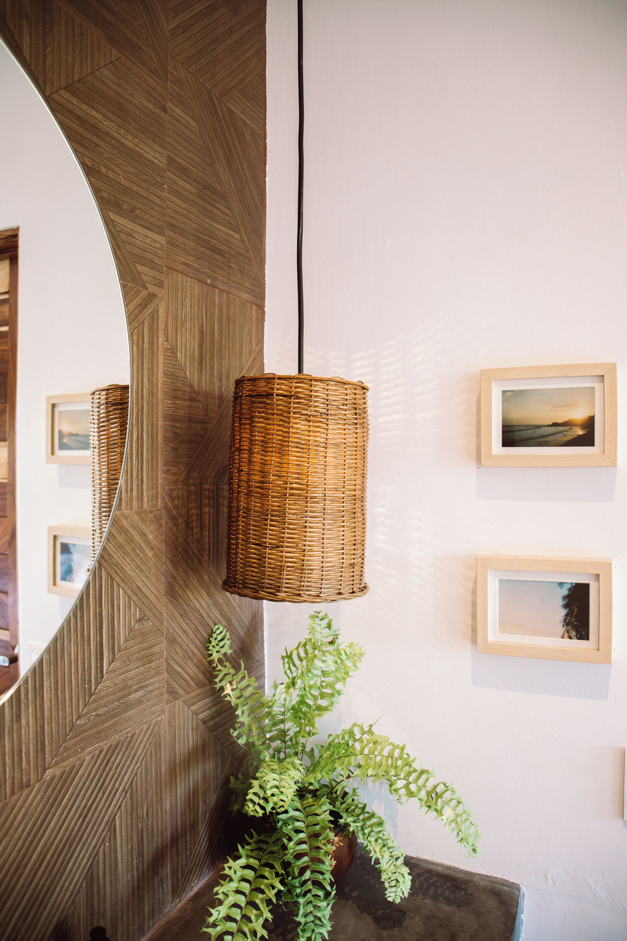 Un interior moderno con un panel de madera, una lámpara colgante de mimbre, cuadros enmarcados y una planta en maceta.