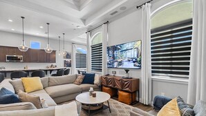 A modern living room with a sectional sofa, a round coffee table, and a dining area with a kitchen in the background. - The Executive Retreat at Westberry (Madera)