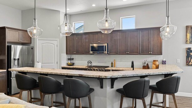 A modern kitchen with dark wooden cabinets, a stainless steel refrigerator, a built-in oven, and a large island with bar stools. - The Executive Retreat at Westberry (Madera)