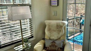 A cozy room with a large window, a chair with a cushion, a floor lamp, and a rug.