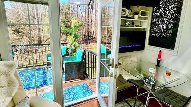 A room with a glass door leading to a patio with a blue patterned rug, a wicker sofa, and a glass table with a lava lamp.
