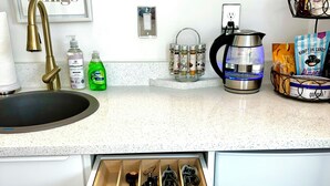 A kitchen with a sink, faucet, countertop, and a drawer with utensils.