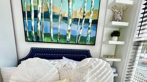 A bedroom with a bed, pillows, a painting, and a window with blinds.