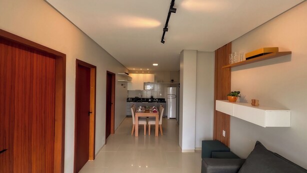A modern kitchen with white cabinets, a dining table, and a built-in oven. - Apto com Piscina e 2 su tes a 100m da Praia (Japaratinga)