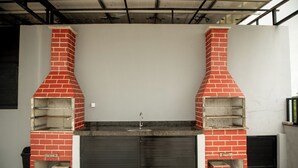 A kitchen with two brick ovens, a sink, and a closed door. - Apto com Piscina e 2 su tes a 100m da Praia (Japaratinga)