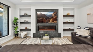 A modern living room with a fireplace, a large flat-screen TV, and built-in shelves. - Oasis at Pecan Valley l Resort Access Included (Hurricane)