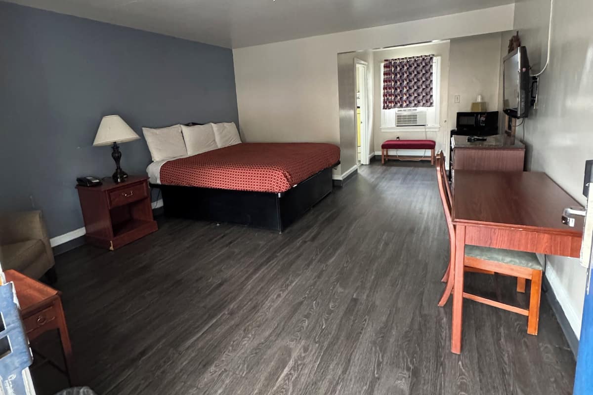 A hotel room with a bed, a desk, a chair, a lamp, and a TV.
