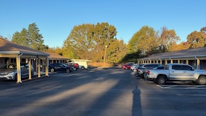 A parking lot with several cars, a building with a covered walkway, and trees in the background. - The Executive Inn (Danville)
