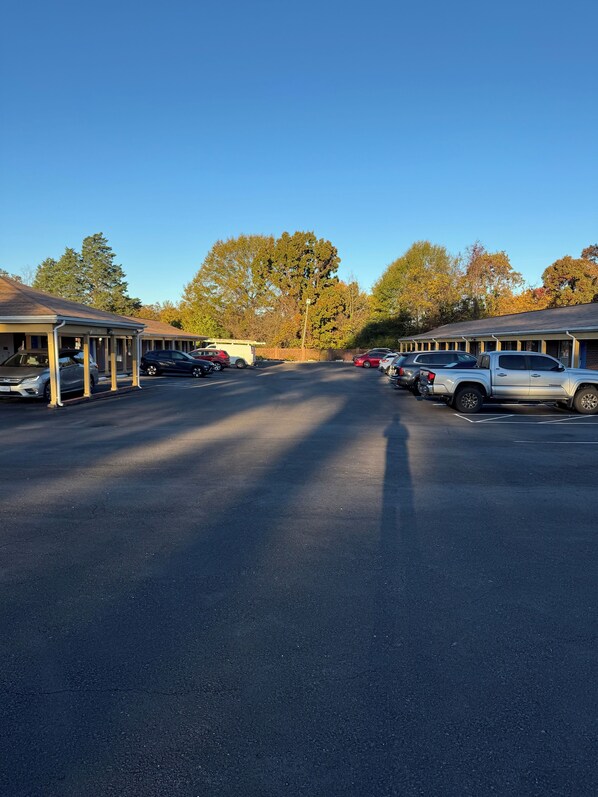 A parking lot with several cars, a building with a covered walkway, and trees in the background. - The Executive Inn (Danville)