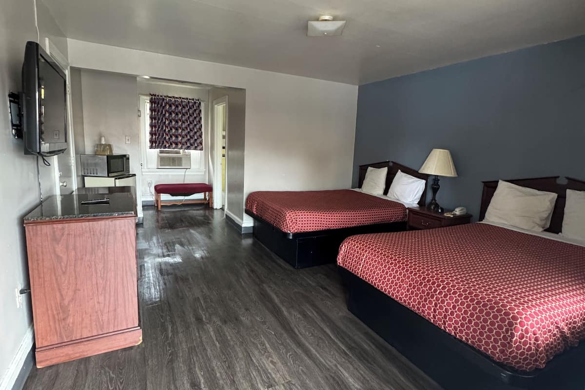 A hotel room with two beds, a TV, a desk, and a trash bin.