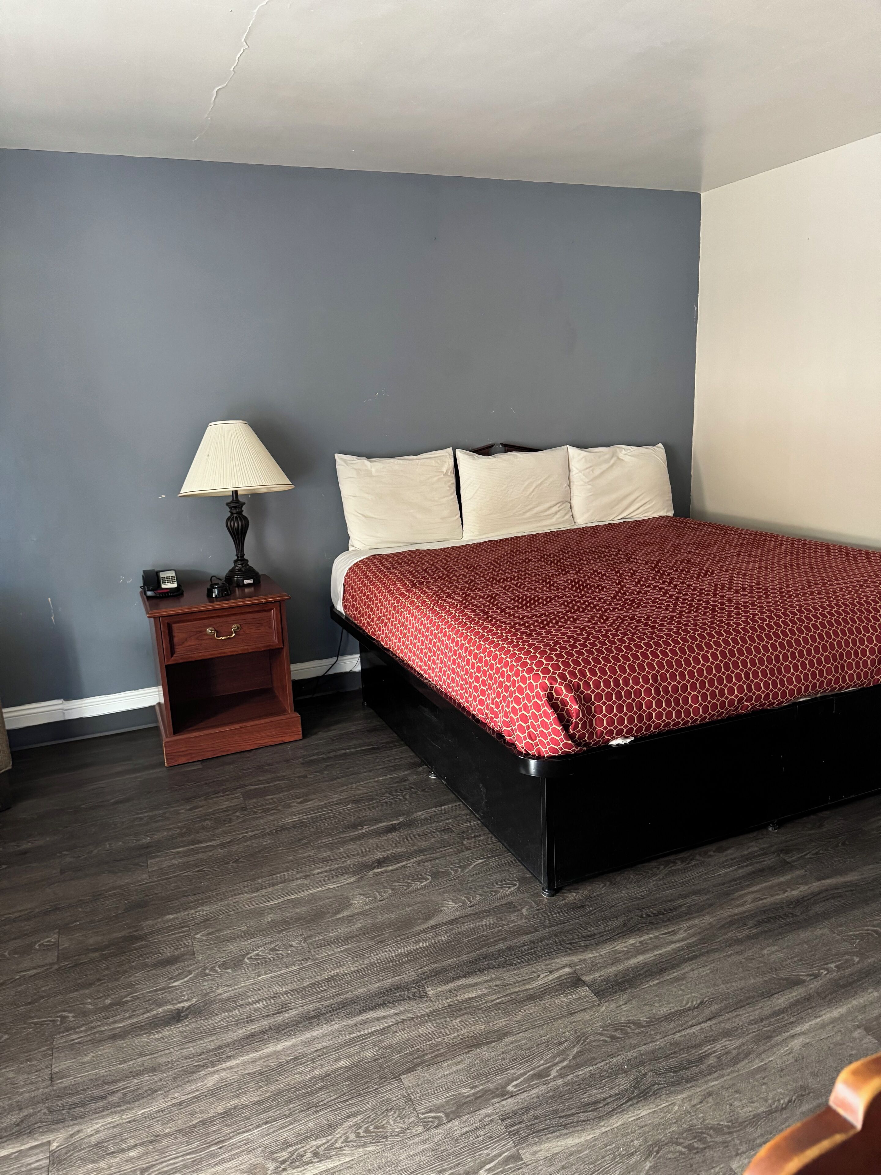 A bedroom with a bed, a nightstand, a lamp, and a wooden floor.