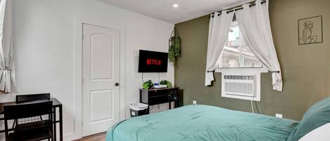Una camera da letto con un letto, una scrivania, una sedia, una televisione e una ventola a soffitto.