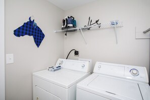 A laundry area with two white front-loading washers and dryers, a blue and black checkered cloth, and a shelf with cleaning supplies.